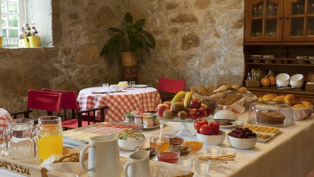 A breakfast buffet with various fruits, pastries, and beverages on a table in a rustic stone-walled room. - Quinta do Casal de S. Miguel de Soutelo (Vila Verde)