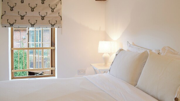 A bedroom with a bed, a window with a view of greenery, a bedside table with a lamp, and a wooden ceiling beam. - 1 bedroom accommodation in Baschurch (Baschurch)