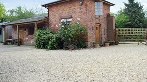 A brick building with a gravel driveway, wooden doors, and a fenced area. - 1 bedroom accommodation in Baschurch (Baschurch)