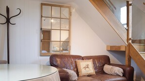 A brown leather sofa with two pillows, a glass table, a wooden-framed window, and a wooden staircase. - 1 bedroom accommodation in Baschurch (Baschurch)