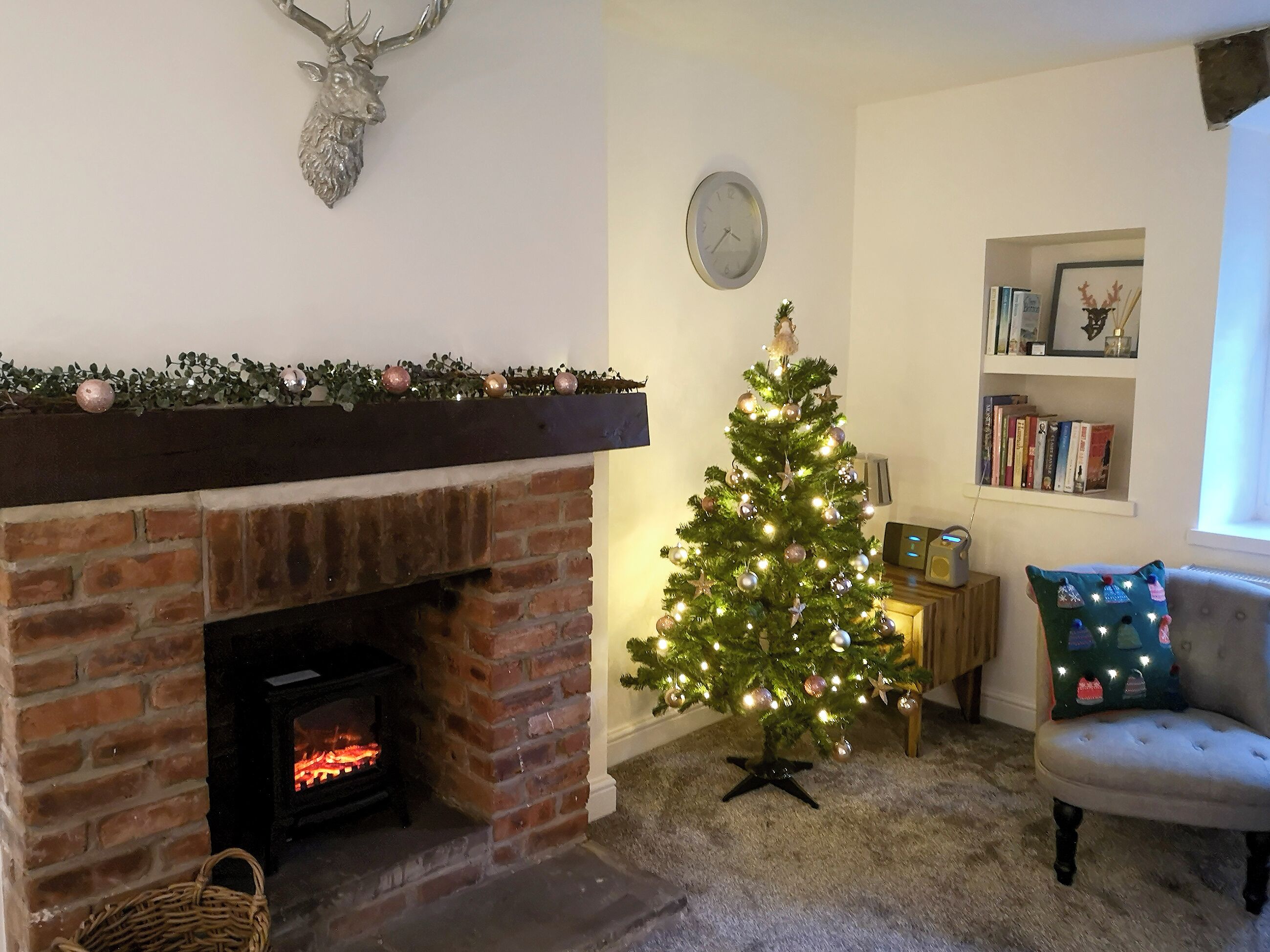 A cozy living room with a brick fireplace, a small Christmas tree, and a bookshelf.