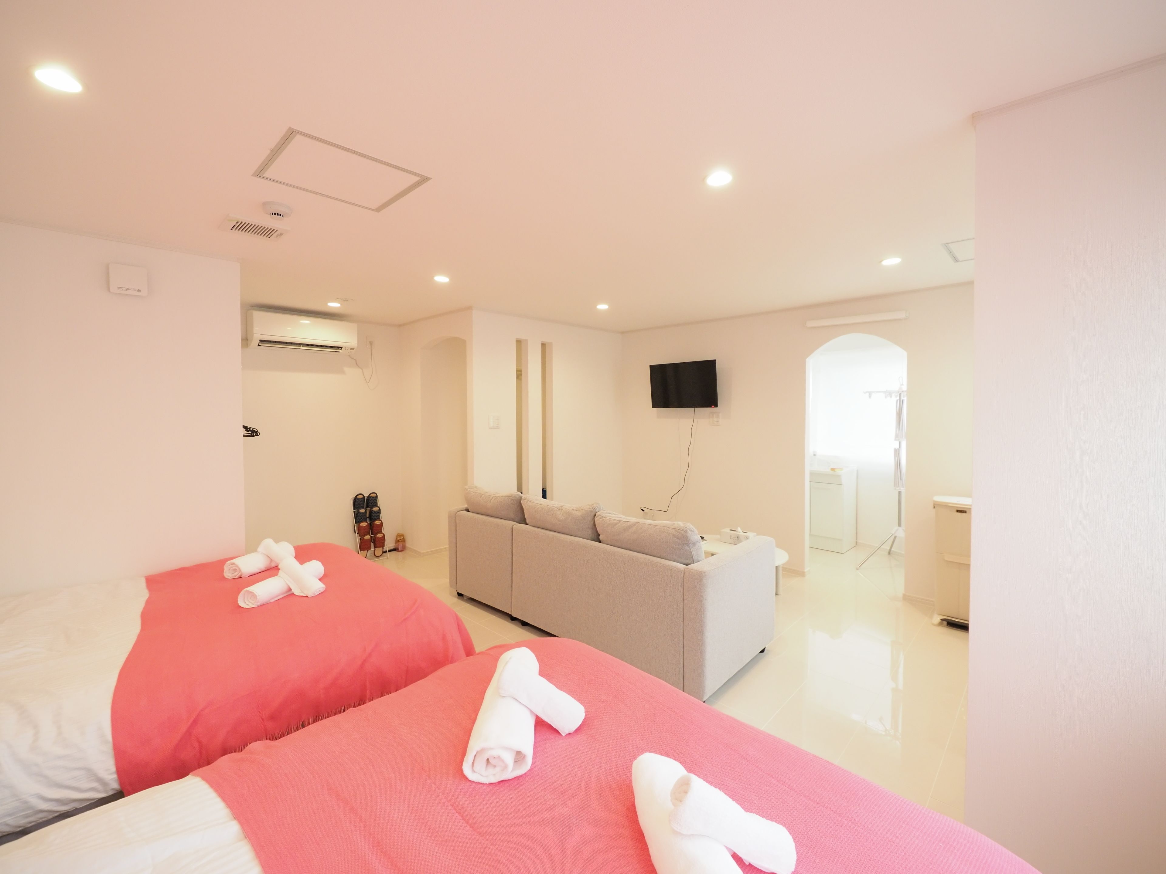 A hotel room with two beds, a grey sofa, a TV, and a bathroom visible through an open door.