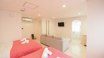 A hotel room with two beds, a grey sofa, a TV, and a bathroom visible through an open door.