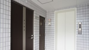 A hallway with a tiled wall, a door, and an elevator. - Kukuru House (Naha)