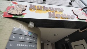 A hotel entrance with a sign reading "Kukuru House" and a row of room signs labeled 1F to 5F. - Kukuru House (Naha)