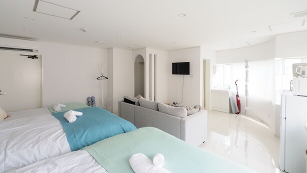 A modern hotel room with two beds, a flat-screen TV, a sofa, and a kitchenette. - Kukuru House (Naha)