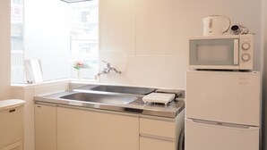 A compact kitchen with a stainless steel sink, a microwave, and a refrigerator. - Kukuru House (Naha)