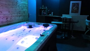 Une pièce avec un jacuzzi, un mur en bois, une porte, un coin bar et une chaise.