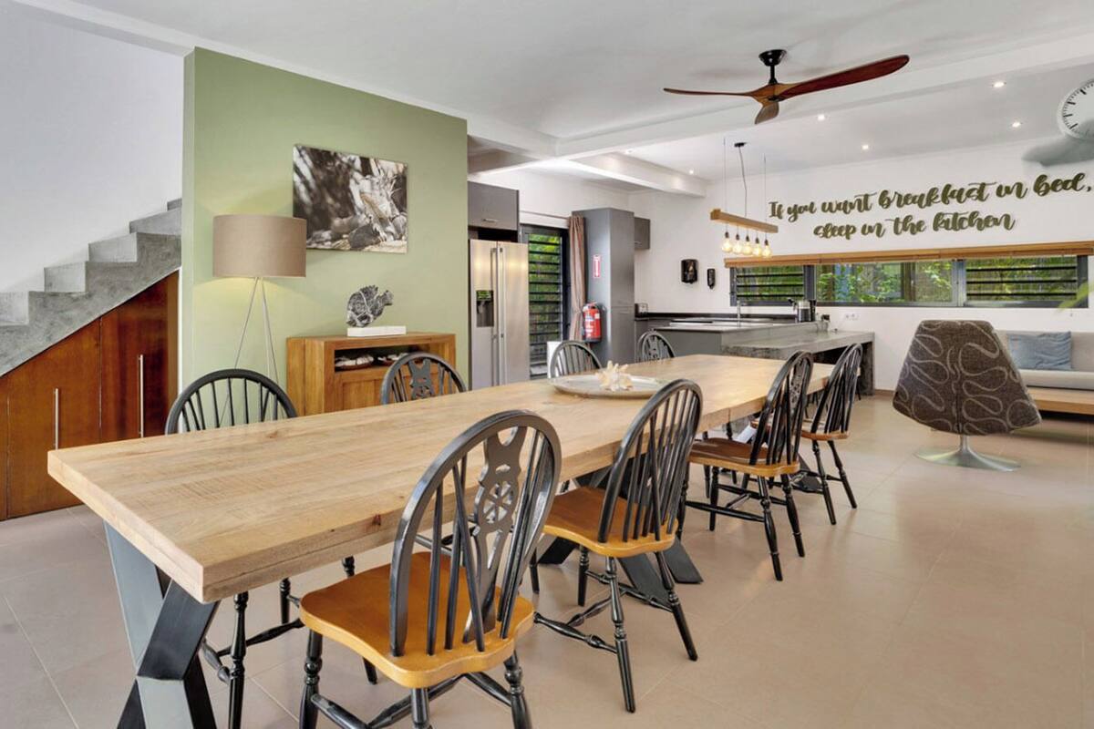 A modern kitchen with a dining area, featuring a wooden table and chairs, a staircase, and a ceiling fan.