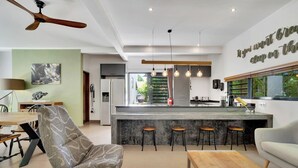 A modern kitchen with a central island, bar stools, and a dining area with a patterned chair and a wooden table. - Deluxe Boutique Apartments Sonrisa Bonaire – Adults only (Kralendijk)