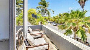 A balcony with three wooden chairs and a view of palm trees and a street. - Deluxe Boutique Apartments Sonrisa Bonaire – Adults only (Kralendijk)