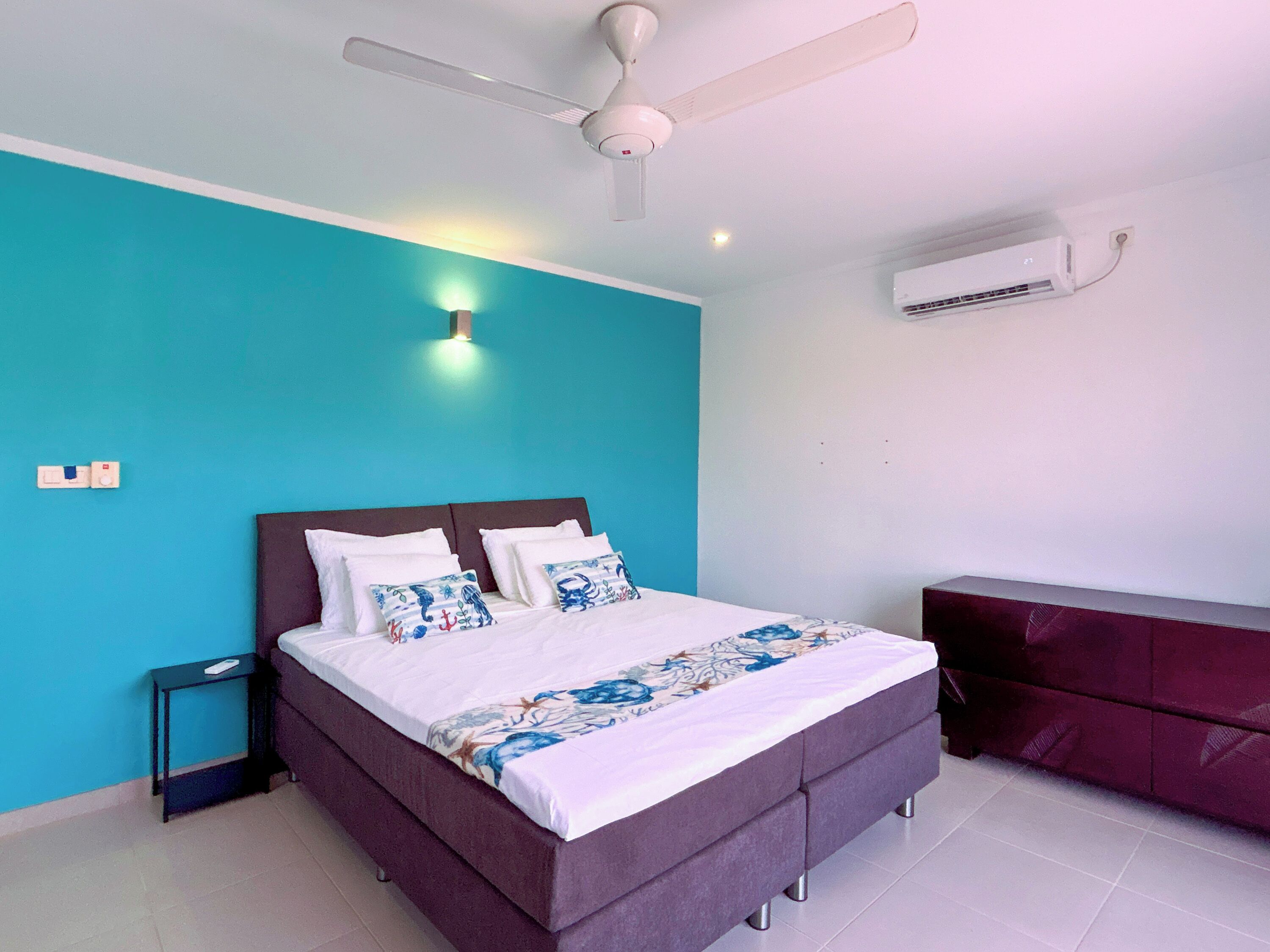 Une chambre à coucher comprenant un lit, une table de chevet, un ventilateur de plafond, un appareil de climatisation et une armoire rouge.