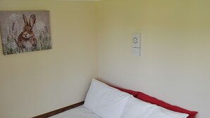 Een slaapkamer met een bed, witte beddengoed, een rode hoofdbord en een schilderij van een konijn aan de muur.