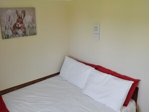 A bedroom with a bed, white bedding, a red headboard, and a painting of a rabbit on the wall. - 2 bedroom accommodation in Stalham (Stalham)