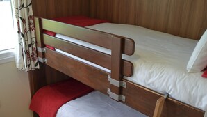 Een stapelbed met een rode deken en witte lakens, een houten hoofdbord en een raam met gordijnen met een patroon.