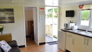 Een kleine keuken met een magnetron, broodrooster en spoelbak. Een houten deur leidt naar een balkon met uitzicht op groen.
