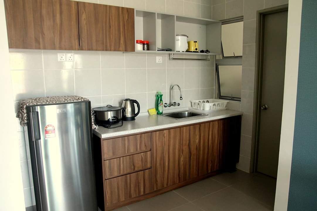 A compact kitchen with wooden cabinets, a stainless steel refrigerator, a kettle, a coffee maker, and a sink.
