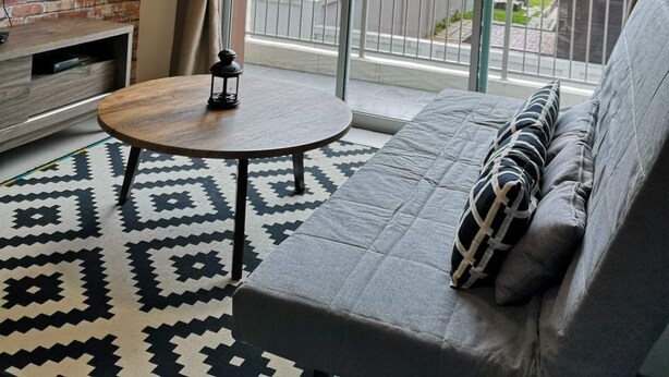 A living room with a sofa, a coffee table, and a TV. There is a large window with curtains, and a brick wall behind the TV. - VgoCameron Home (Tanah Rata)