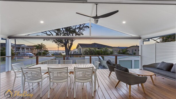 A covered outdoor area with a table and chairs, a sofa, and a ceiling fan. - Twilight on Sunset Beach - Soldiers Point - Amazing sunset views (SOLDIERS POINT)