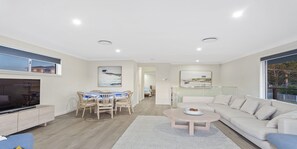 A modern living room with a flat-screen TV, a dining area with a table and chairs, a sofa, and a coffee table.