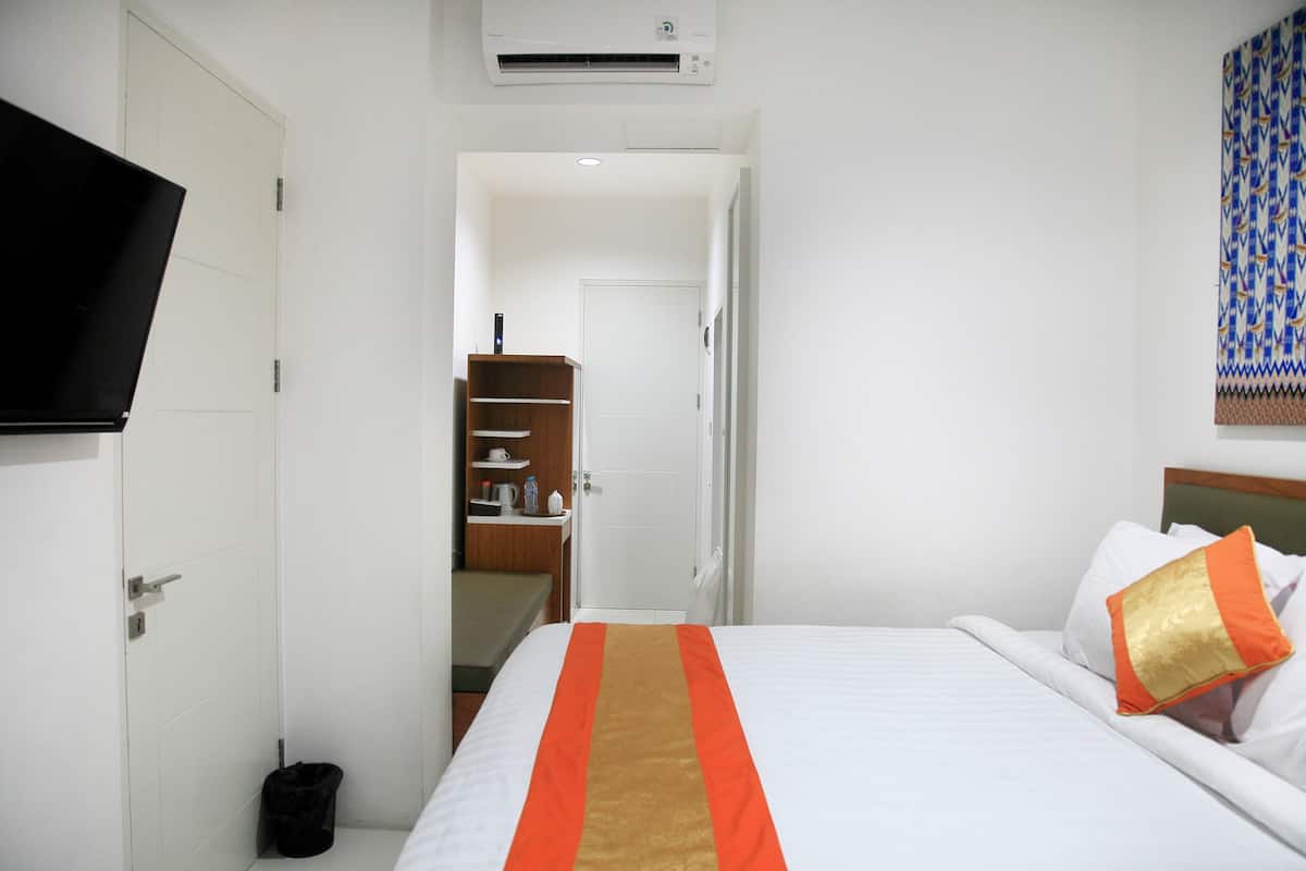 A hotel room with a bed, a television, a door, and a small trash bin.