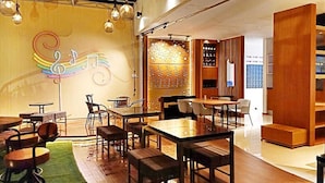 A restaurant with wooden tables and chairs, a neon music sign, and a decorative wall. - Arawa Traveller's Inn Makassar - Hostel (Makassar)