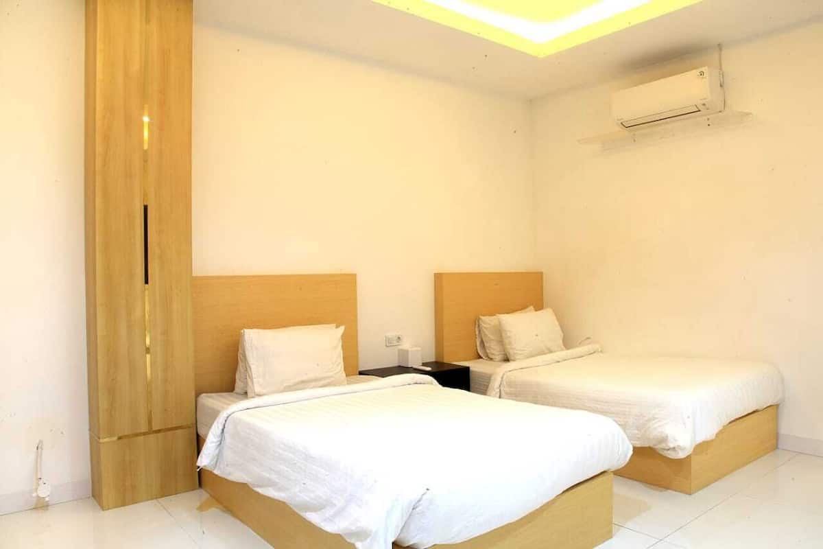 A hotel room with two single beds, a wooden wardrobe, a nightstand, and an air conditioning unit on the wall.