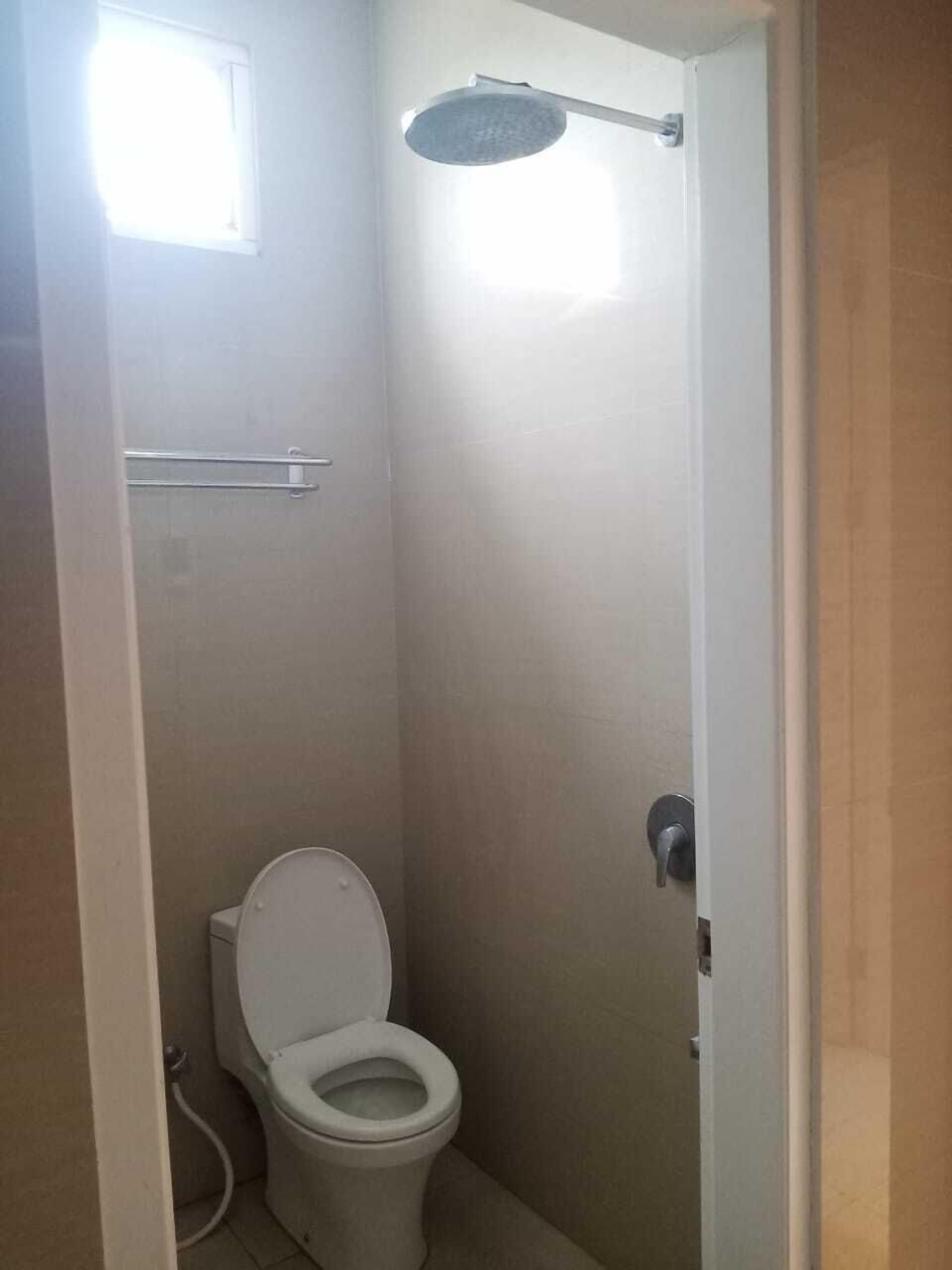 Un baño pequeño y cerrado con inodoro, cabezal de ducha y ventana.