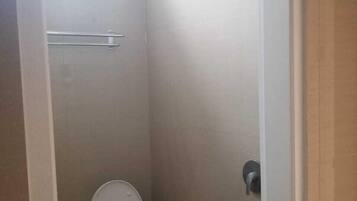 Un baño pequeño y cerrado con inodoro, cabezal de ducha y ventana.