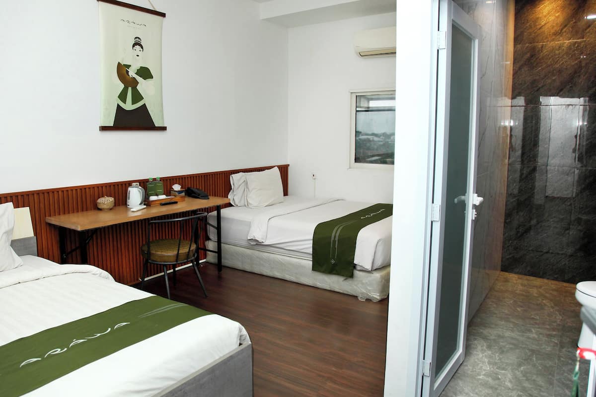 A hotel room with two beds, a desk, a chair, and a bathroom with a shower.