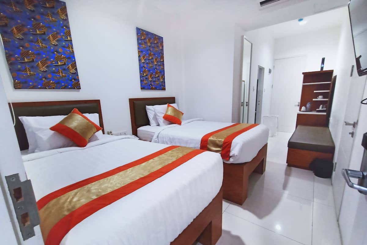 A hotel room with two beds, each with white bedding and red and gold accents, a wooden bench, and a small staircase.