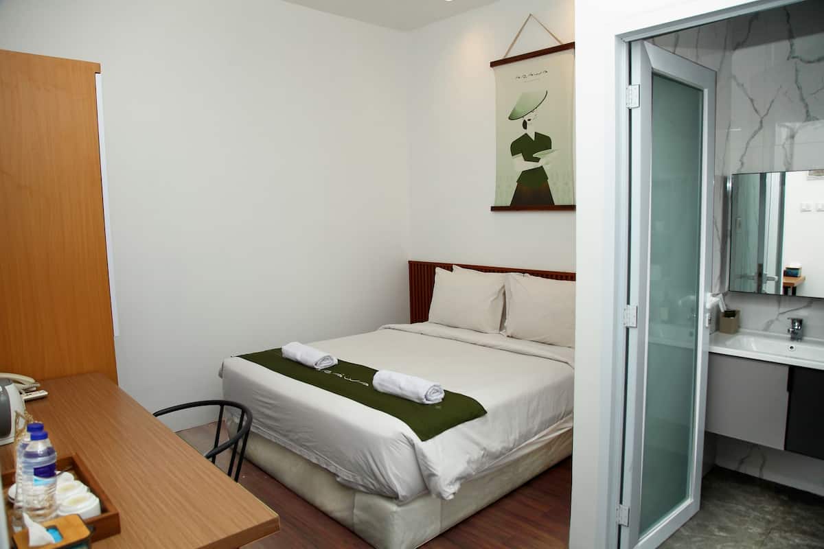 A hotel room with a bed, bedside table, and a bathroom with a sink and mirror.