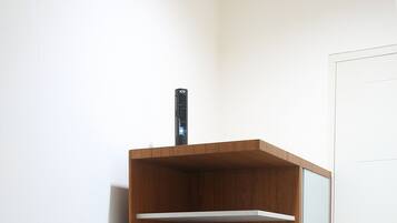 A compact room with a wooden cabinet, a small table with a kettle, cups, and a water bottle.