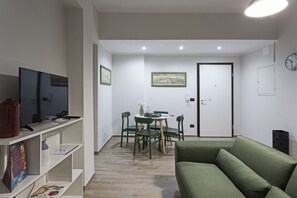 Un soggiorno con un divano verde, una televisione, un tavolo da pranzo con sedie e una porta con un orologio.