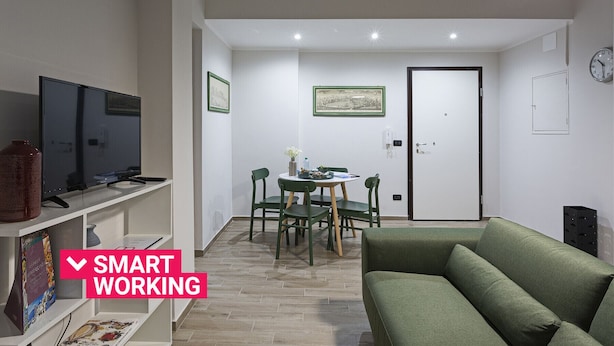Una sala moderna con un sofá verde, un comedor con mesa y sillas, y un televisor sobre una estantería.