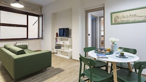 Una sala de estar moderna con un sofá verde, una mesa de comedor con sillas, un televisor en un estante y un cuadro en la pared.