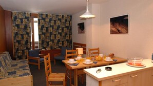 Ein gemütliches Zimmer mit einer Holzsofa, einem Esstisch mit Stühlen und einer kleinen Küchenzeile.