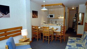 Ein gemütlicher Wohnraum mit Esstisch, Stühlen, einer Couch, einer kleinen Küchenzeile und einer Holzbank.