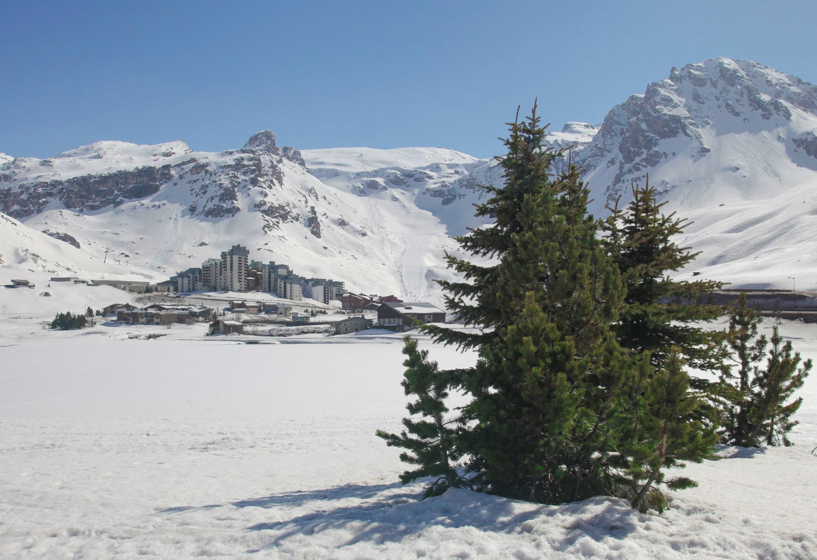 Paisaje nevado con una montaña, un edificio pequeño y un pino.