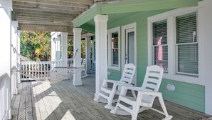 A porch with white rocking chairs, a wooden deck, and a green building facade. - Brown Dog by the Sea: Soundside, Private Pool, Spa (Corolla)