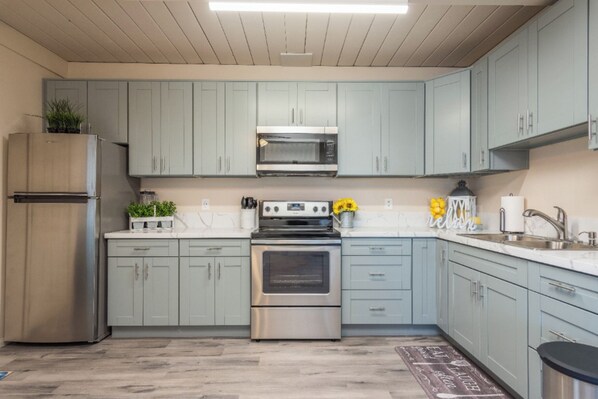 A kitchen with light blue cabinets, stainless steel appliances, and a marble countertop.