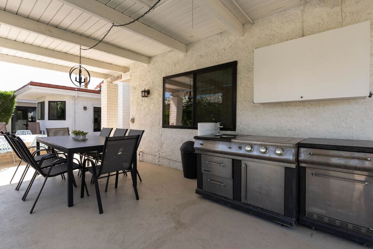Um pátio externo com mesa e cadeiras, churrasqueira e um quadro branco na parede.