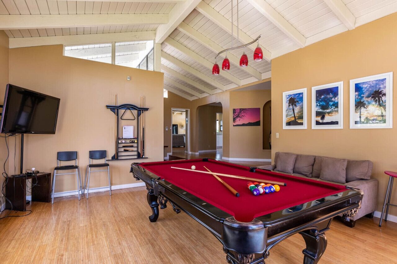 A pool table with pool balls, a television, and a sofa in a room with wooden floors and a high ceiling.