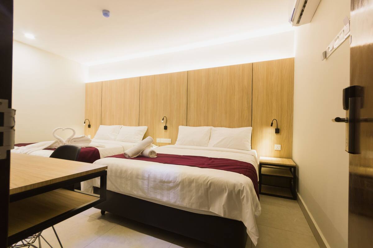 A hotel room with two beds, a wooden headboard, bedside tables with lamps, and a desk.