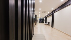 Um corredor moderno com um banco, parede listrada em preto e branco e uma porta de vidro no final.
