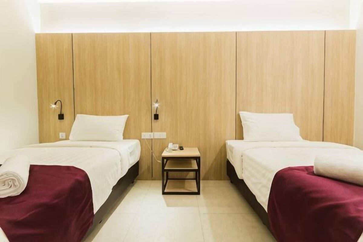 A hotel room with two beds, a wooden wardrobe, a small table with a phone, and a light-colored floor.
