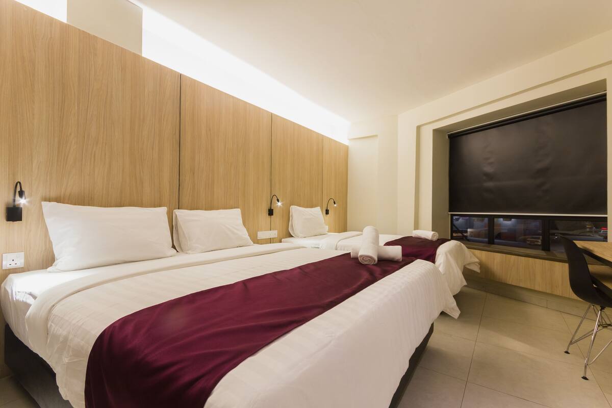 A hotel room with a large bed, two bedside tables, a desk with a chair, and a large window.