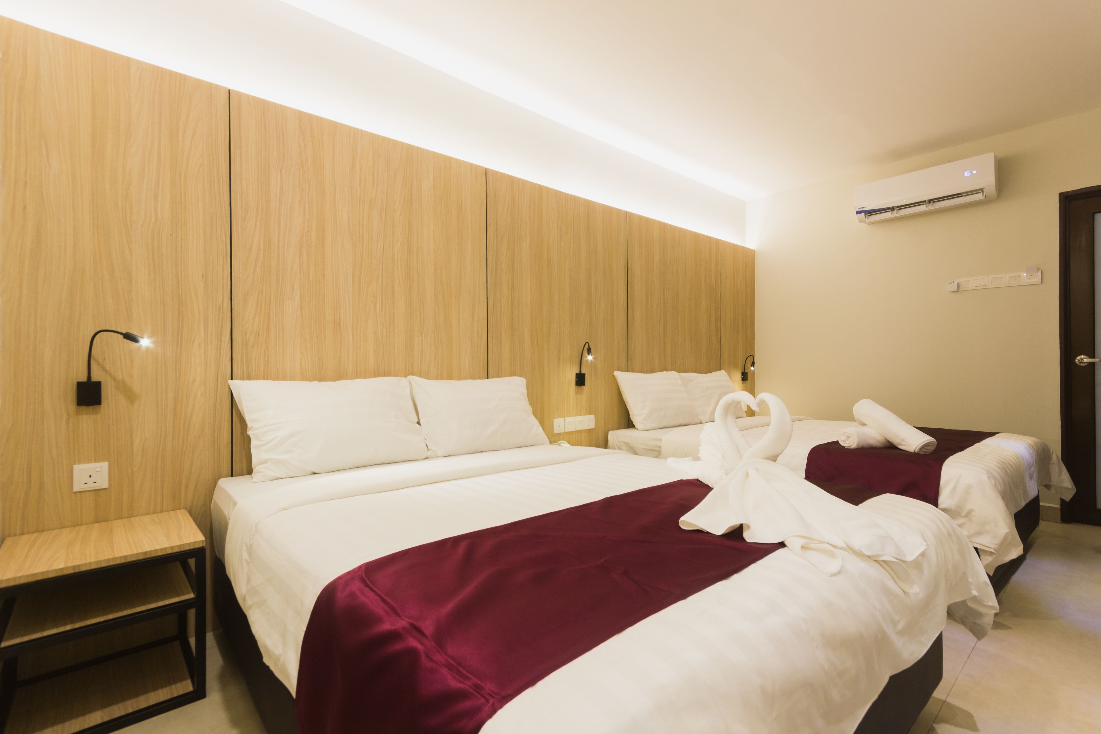A hotel room with two beds, a wooden wall, an air conditioning unit, and a bedside table.
