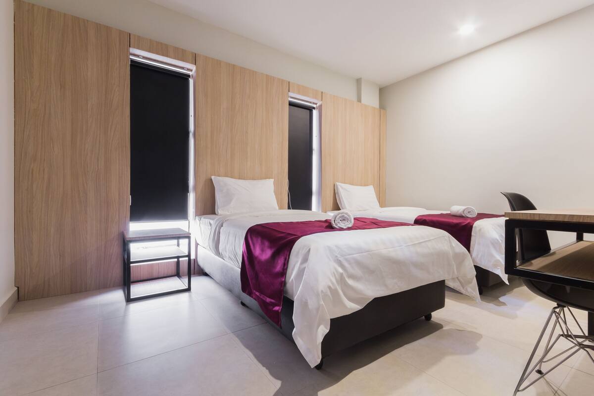 A modern hotel room with two beds, a desk, and a wardrobe.