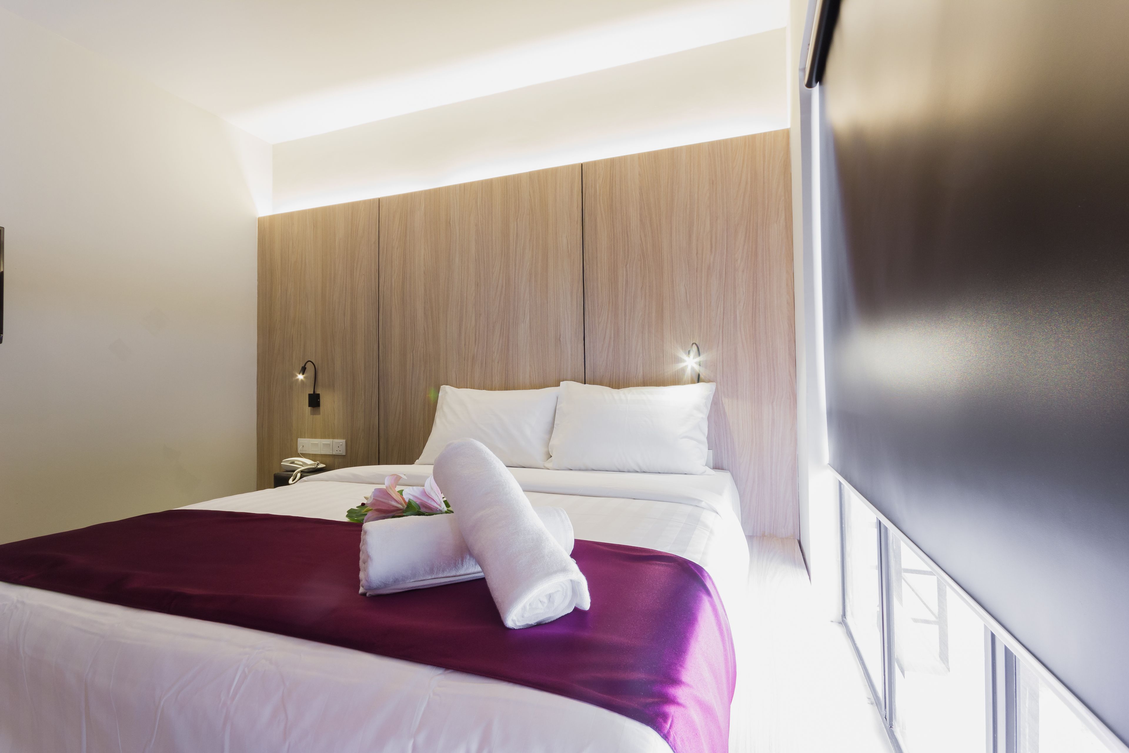 A hotel room with a large bed, a wooden panel wall, a bedside table with a phone, and a window with a view.